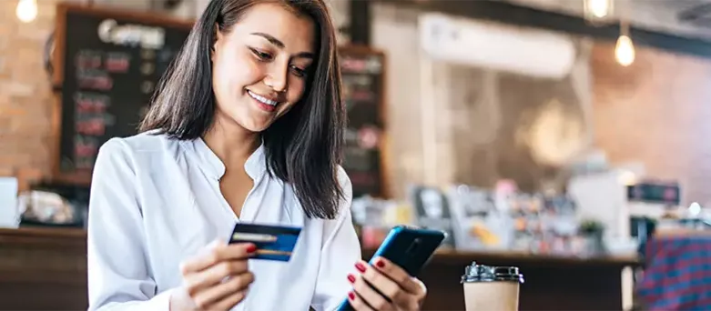 Mujer realizando una transacción digital con celular y tarjeta en cafetería